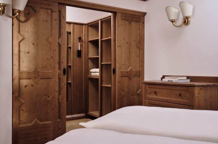 Cozy rustic bedroom with a bed, nightstand, closet, and warm wood accents, featuring wall lamps and white walls.