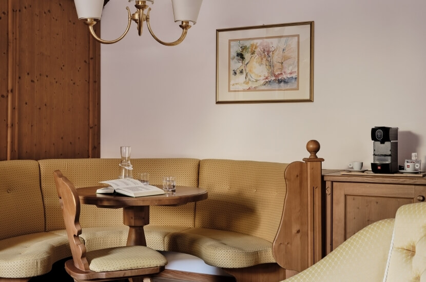 Cozy dining area with yellow L-shaped couch, dark wood table, two upholstered chairs, and warm lighting from a faux-crystal lamp.