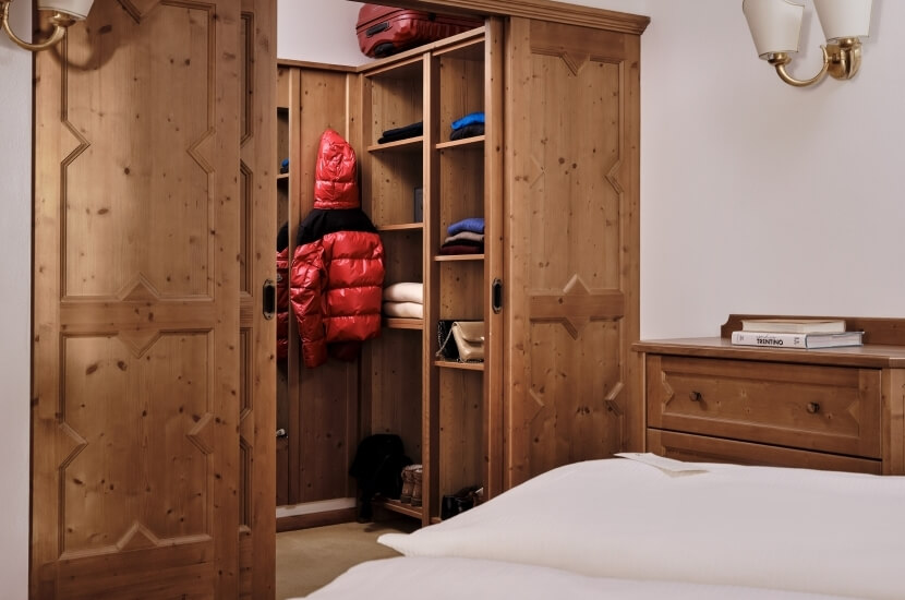 A minimalist bedroom with a closet, dresser, and bed, featuring a red puffer jacket and suitcase for color.