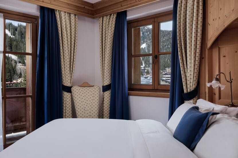 Camera da letto accogliente con un grande letto, finestre con tende blu e un comodino decorato in stile rustico.