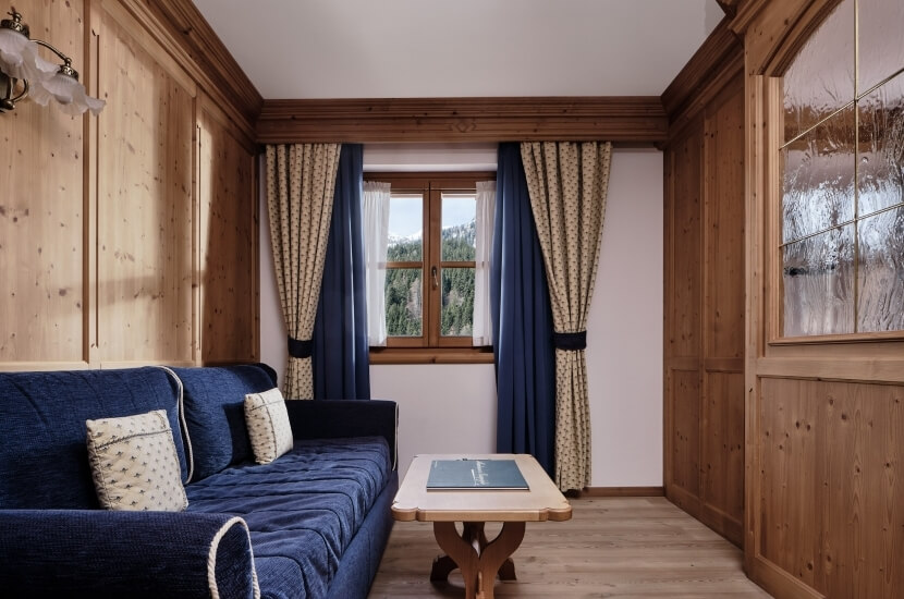 Una stanza accogliente con un divano blu, tavolino in legno, finestre con tende e un lampadario elegante.