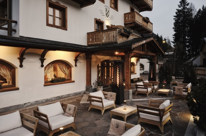 Das Bild zeigt die Außenansicht eines Hotels mit einer einladenden Terrasse, Holzdetails und einer ruhigen Atmosphäre bei Sonnenuntergang.