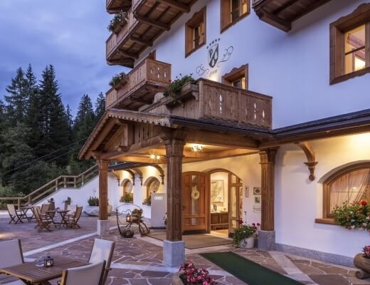 Edificio in stile alpino bianco con accenti marroni, patio accogliente e foresta verde sullo sfondo, atmosfera serena.