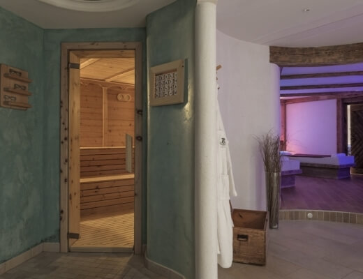 Sauna z drewnianymi ławkami i białym szlafrokiem, obok pokój relaksacyjny z oknem i rośliną w rogu.