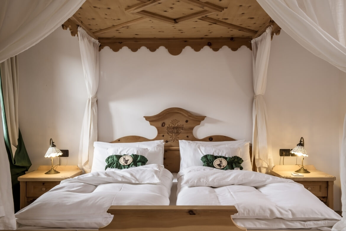 Ein elegantes Schlafzimmer mit zwei Einzelbetten, weißen Bettlaken, Nachttischen, Holzdecke und weißen Vorhängen.