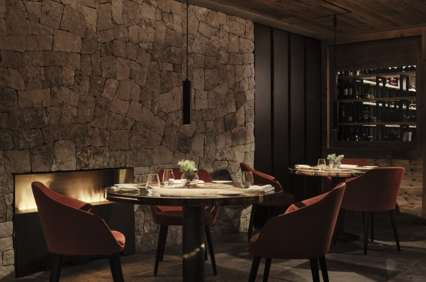 Gemütlicher Restaurantbereich mit zwei runden Tischen, roten Stühlen und einem Kamin im Hintergrund.