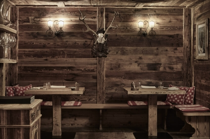 Rustikaler Essbereich mit Holztisch, Bänken, Hirschgeweih, Wandbeleuchtung und gemütlicher Atmosphäre.