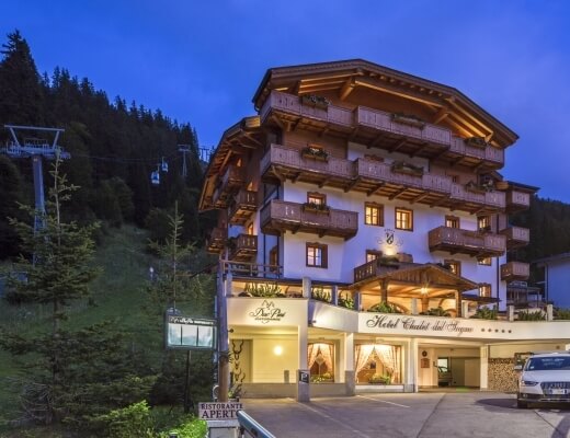 Hotel Chalet del Sogno in montagna, con veicoli bianchi, ristorante e seggiovia sullo sfondo di alberi verdi e cielo blu.