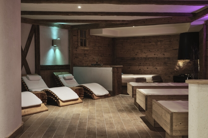 Ein ruhiger Wellnessraum mit Holzwänden, Lounge-Stühlen, Behandlungstischen und einer einladenden Atmosphäre.