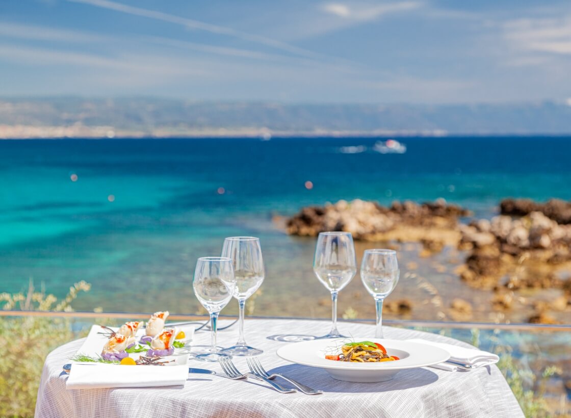 Tavolo con piatti di pasta e frutti di mare, vista sul mare.