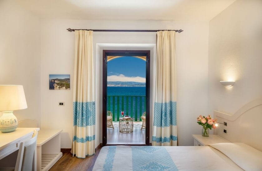 Camera d'hotel con letto, scrivania, balcone e vista mare.