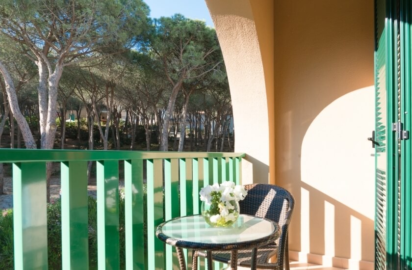 Balcone con ringhiera verde, tavolo di vetro e fiori bianchi.