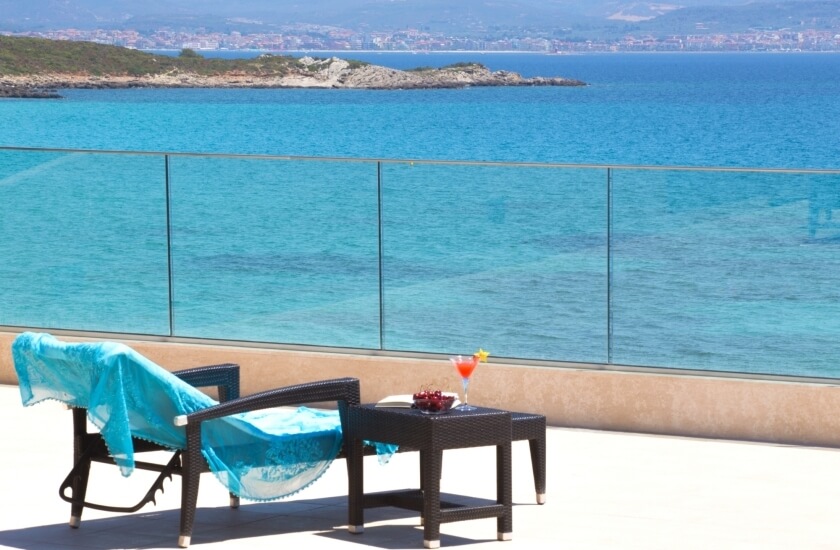Balcone con vista sul mare turchese e cocktail decorato.