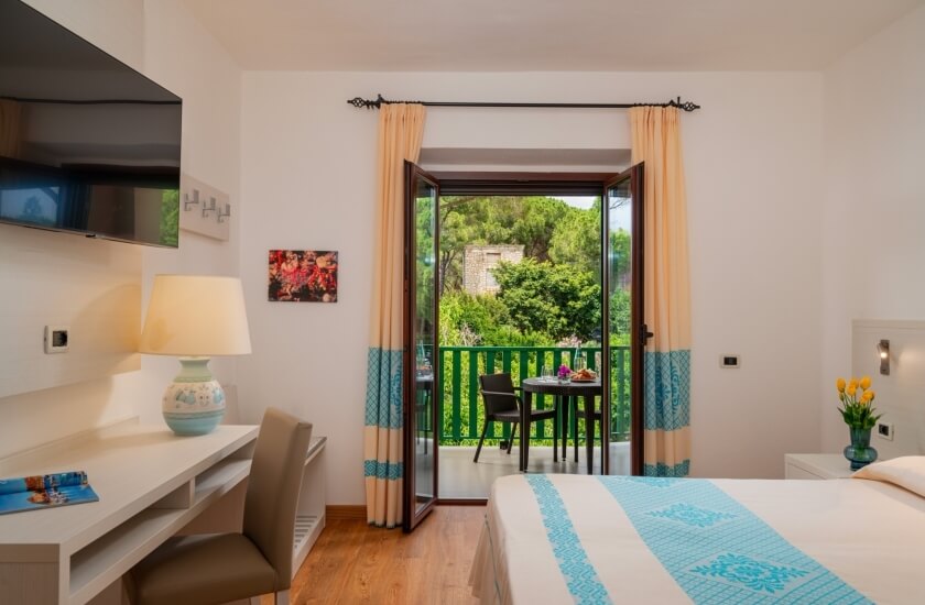 Camera d'hotel con letto, scrivania, balcone e vista verde.