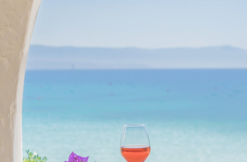 Un bicchiere di vino rosato davanti a un oceano turchese.