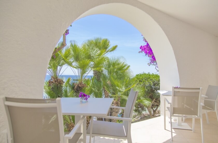 Arco bianco con vista su palme, oceano e fiori viola.
