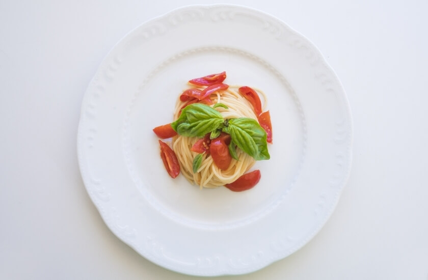 Spaghetti con pomodori a fette e foglie di basilico.