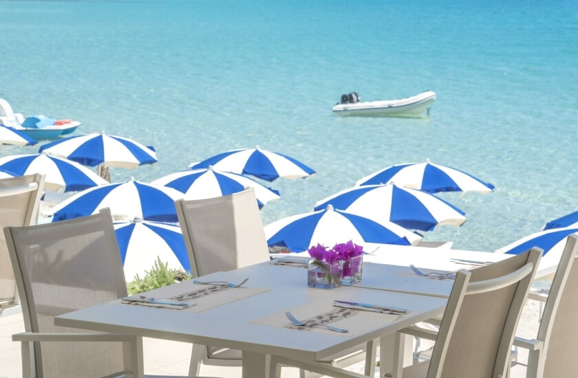 Tavolo bianco con fiori, vista sull'oceano turchese e ombrelloni.