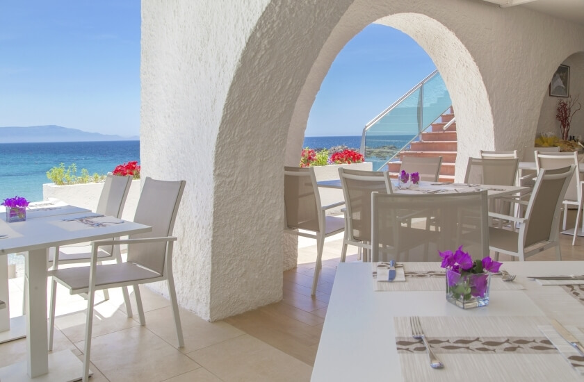 Area pranzo all'aperto con vista sul mare turchese e fiori.