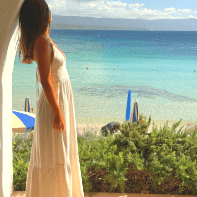 Donna in abito bianco su un balcone, guarda il mare.