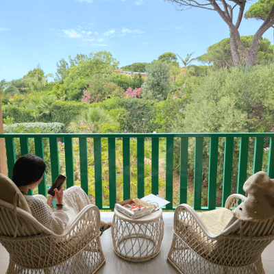 Persona su un balcone con pizza, libro e paesaggio verde.