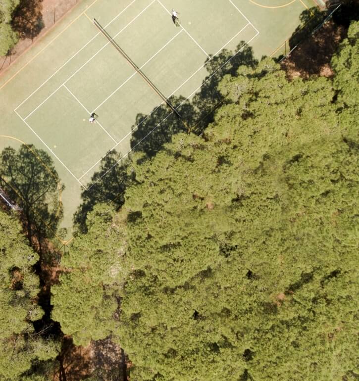 Luftaufnahme eines Tennisplatzes mit zwei Spielern und umgebenden Bäumen.