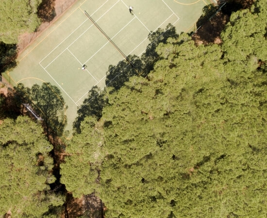 Vista aerea di un campo da tennis con due giocatori e alberi.
