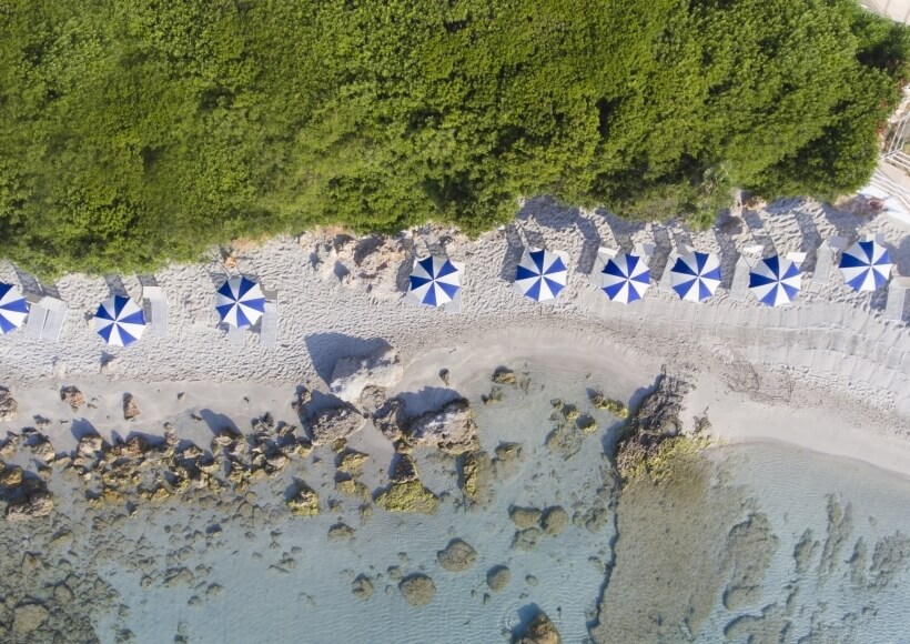 Vista aerea di una spiaggia con ombrelloni e acqua cristallina.