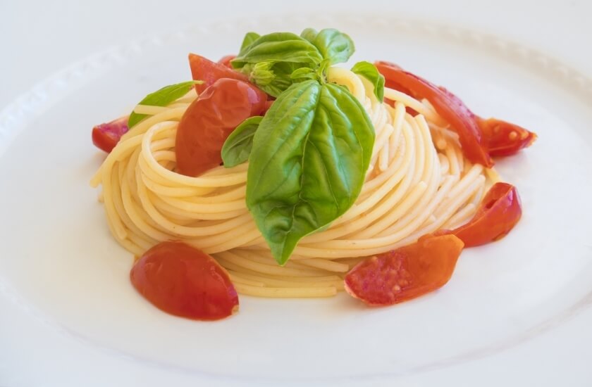 Piatto di spaghetti con pomodorini e foglie di basilico fresco.