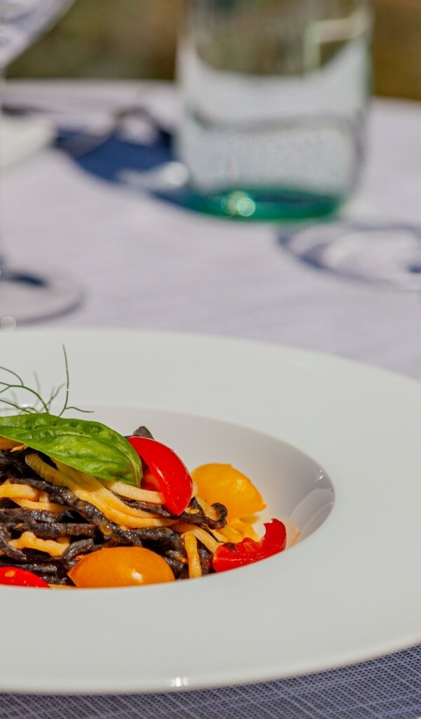 Pasta scura con pomodorini e basilico su un piatto bianco.