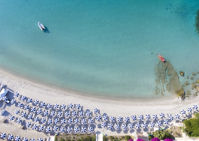 Vista aerea di una spiaggia con ombrelloni e acque turchesi.