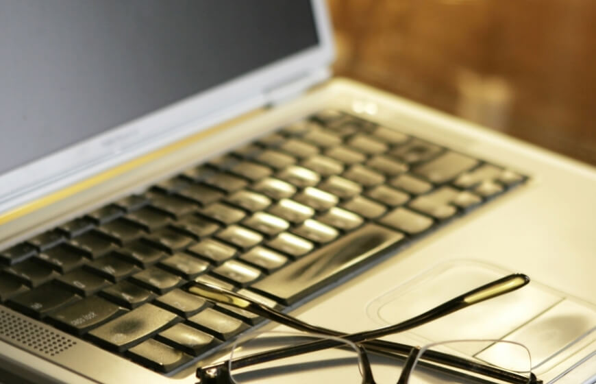 Laptop with black keyboard and eyeglasses on touchpad.   Laptop con tastiera nera e occhiali sul touchpad.