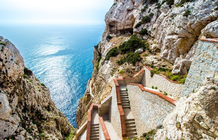 Scalinata in pietra con bordi in mattoni rossi, affacciata sull'oceano blu.