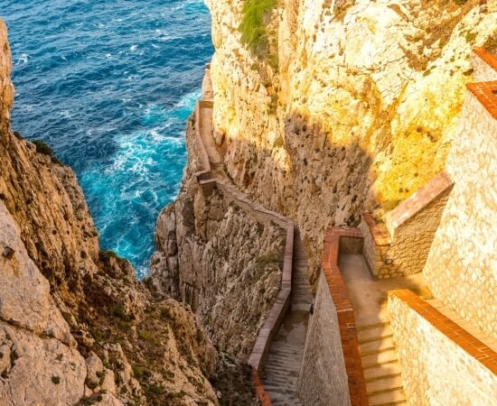 Scalinata di pietra con bordi in mattoni lungo un cliff e acqua blu.
