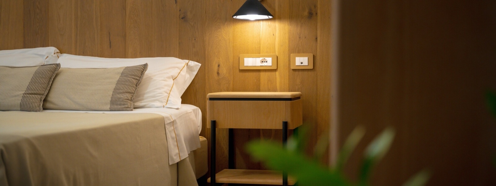 Letto con coperta beige, cuscini a righe e testiera in legno.