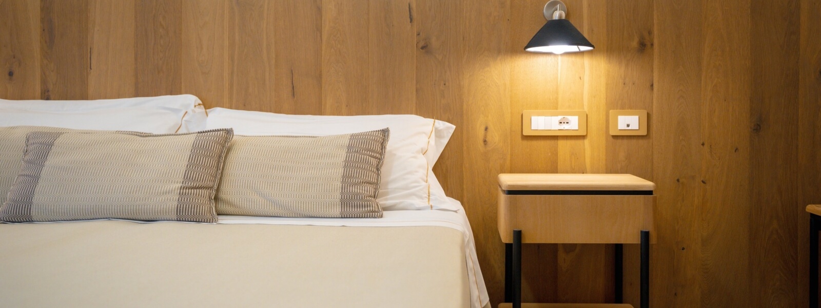 Letto con lenzuola bianche, cuscini decorativi e comodino.