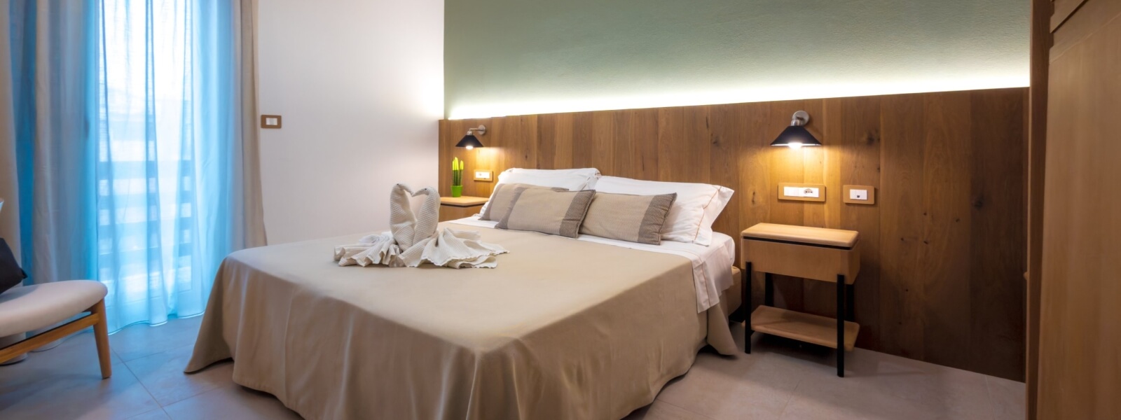 Hotel room with swan-shaped towels, neutral linens, and green walls.