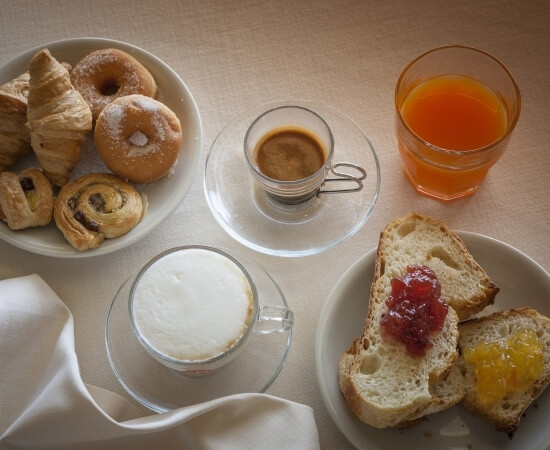 Colazione con croissant, ciambelle, caffè, succo d'arancia e pane con marmellata.
