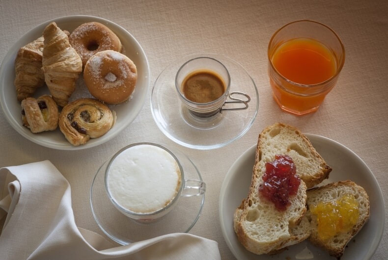 Colazione con croissant, dolci, pane con marmellata, succo d'arancia e caffè.