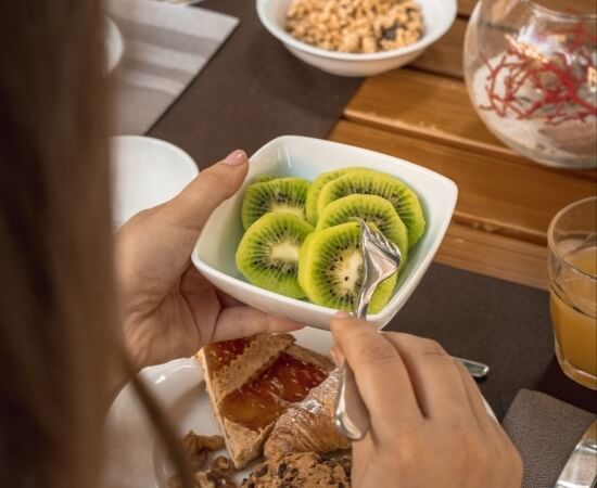 Bowl of sliced kiwis, croissant, jam, orange juice, and coral.   Bowl di kiwi a fette, cornetto, marmellata, succo d'arancia
