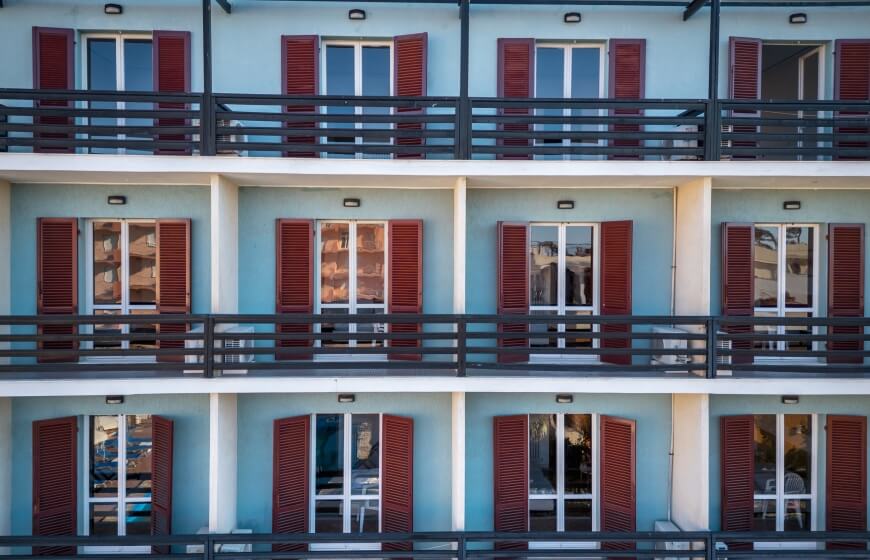 Edificio a più piani con finestre, persiane rosse e balconi.