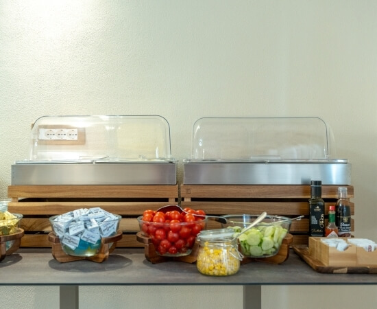Buffet con cibi caldi, pomodorini, cetrioli, mais e condimenti.