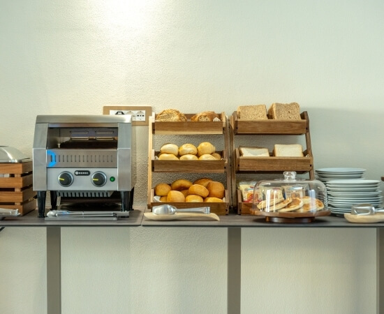 Buffet con tostapane, pane, piatti bianchi e pancake coperti.