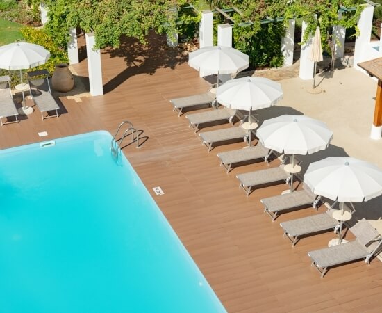 Piscina blu circondata da un deck in legno e ombrelloni bianchi.