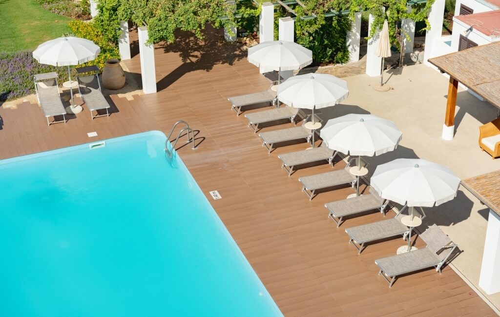 Piscina all'aperto con acqua blu, lettini e ombrelloni bianchi.