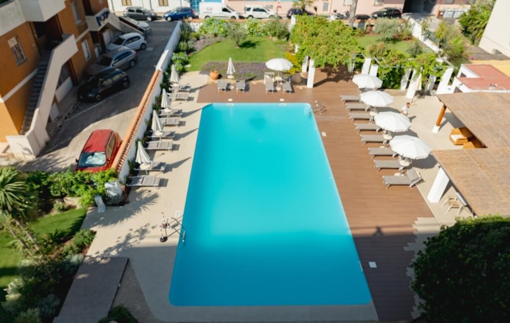 Piscina all'aperto con lettini, ombrelloni e edificio arancione.