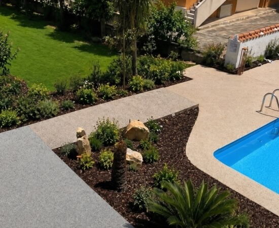Area esterna con piscina, giardino, sentieri e edificio arancione sullo sfondo.