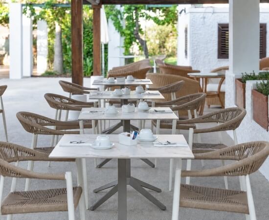 Area pranzo all'aperto con tavoli, sedie e vegetazione verde.