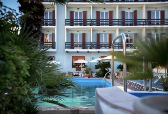 Edificio a più piani con balconi e piscina, circondato da vegetazione.