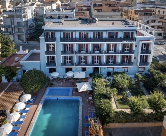 Edificio blu chiaro con persiane rosse, piscina e giardino.